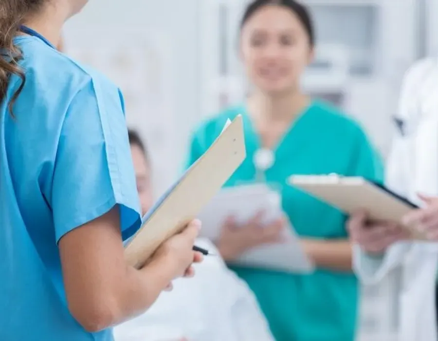 Registered nurse holding clipboard speaking with nursing staff including family nurse practitioner